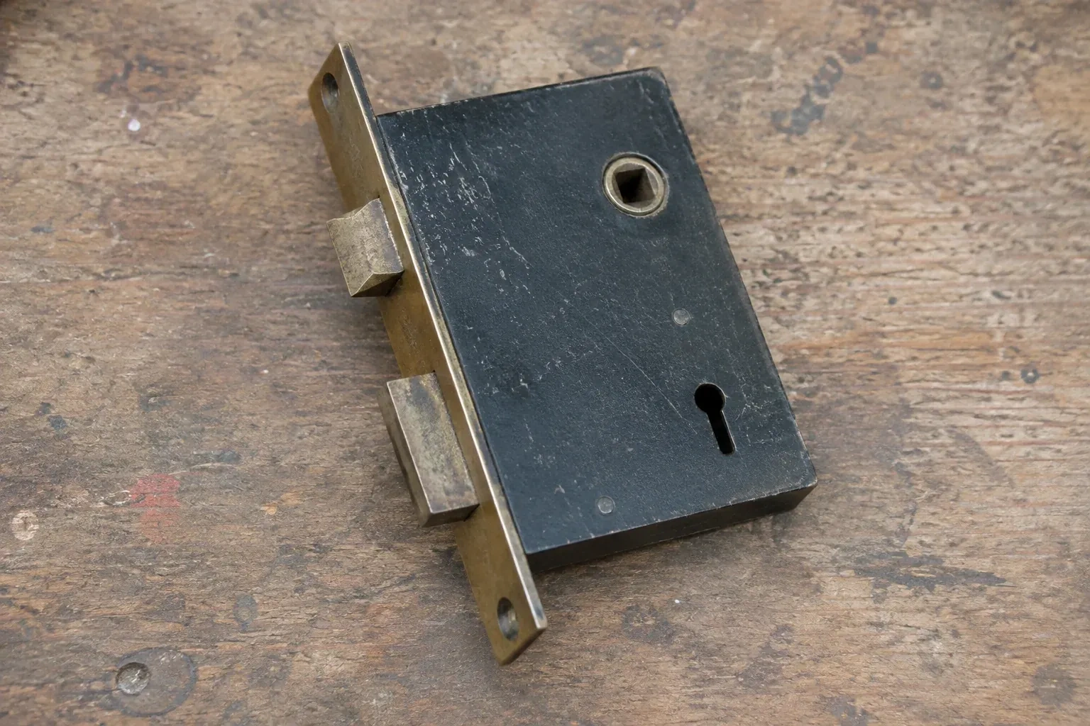 Closed mortise lock case with spindle opening, keyhole, latch and deadbolt on a wooden workbench. — Vintage Mortise Lock Service, Markham