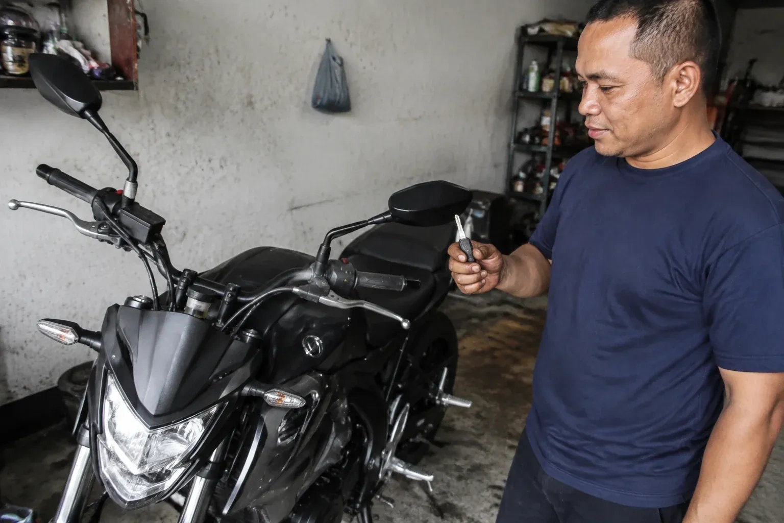 Person holding a key beside a black motorcycle in a garage. — Motorcycle & Scooter Keys, Markham