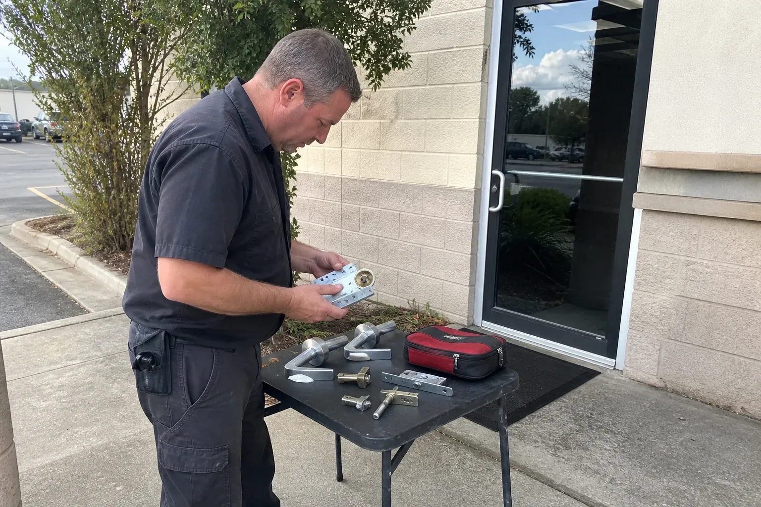 Technician examining detached commercial lock hardware on a table outside a shop entrance. — Business Lockout Service, Markham